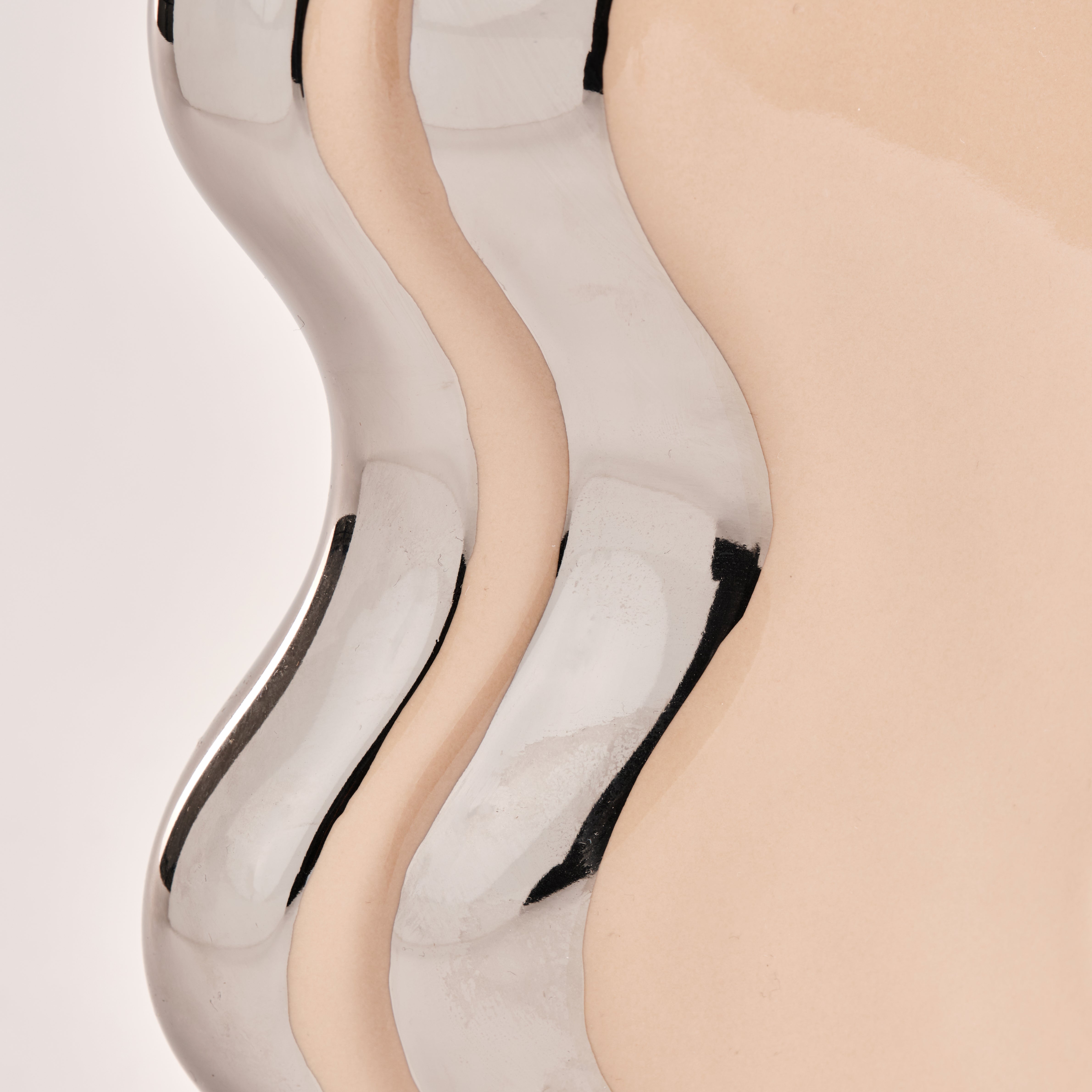 Nahaufnahme der Porzellanvase "Curl" mit ihrem charakteristischen Wellen-Design in glänzendem Chrom und Beige. Die feinen Details und die geschwungene Form unterstreichen das moderne und edle Design dieser exklusiven Vase.