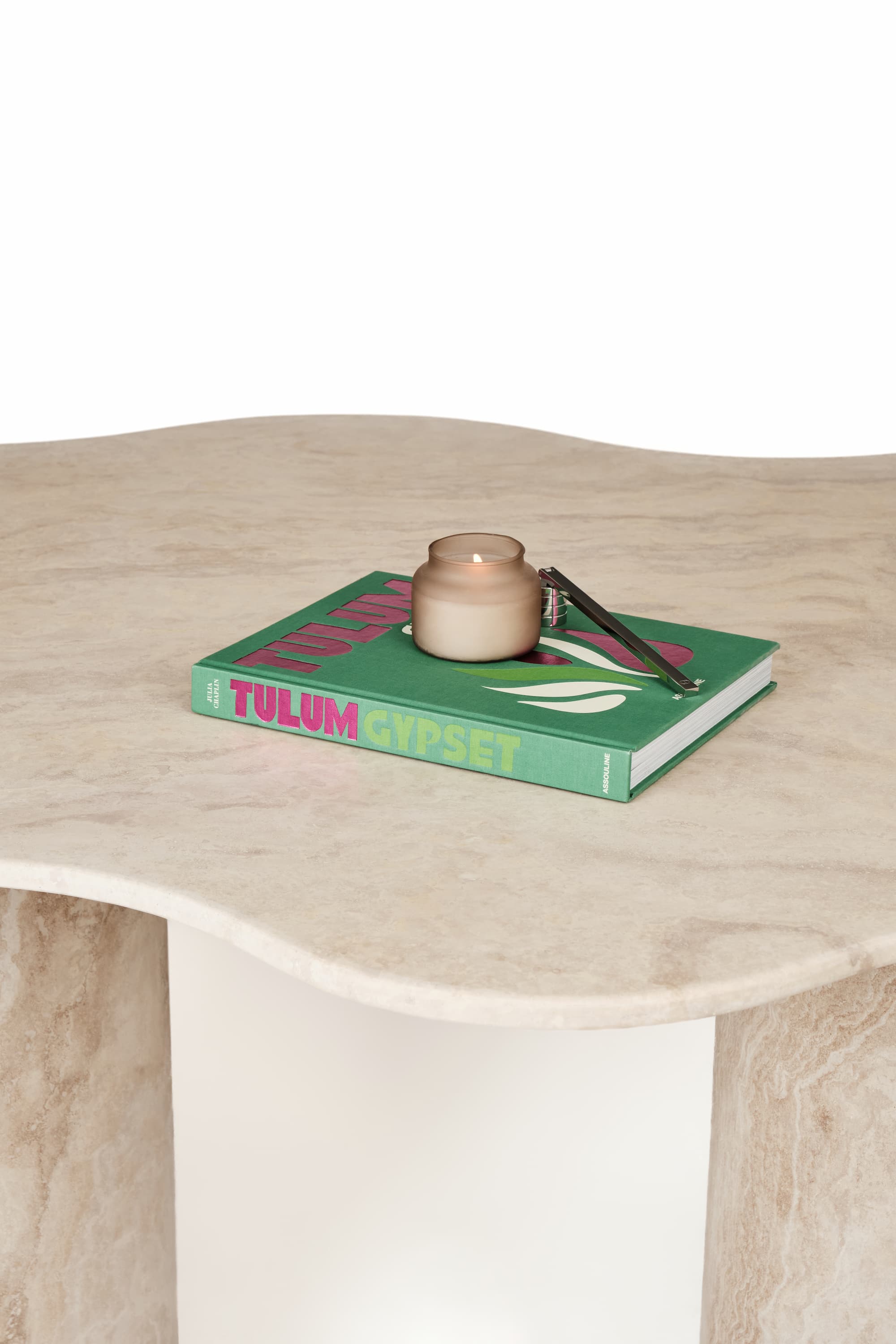 Detailaufnahme des Travertin-Esstischs Organic, dekoriert mit einem grünen Buch, einer beige Kerze und einem Kerzenschneider, perfekt für moderne Wohnräume.