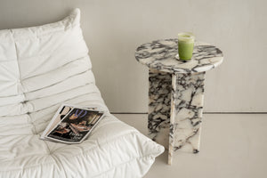 Beistelltisch aus edlem Marmor mit Schwarz-Weiß-Maserung, dekoriert mit einem Glas Matcha-Getränk, neben einem gemütlichen weißen Lounge-Sessel mit Magazin. Perfekt für moderne und elegante Wohnraumgestaltungen.