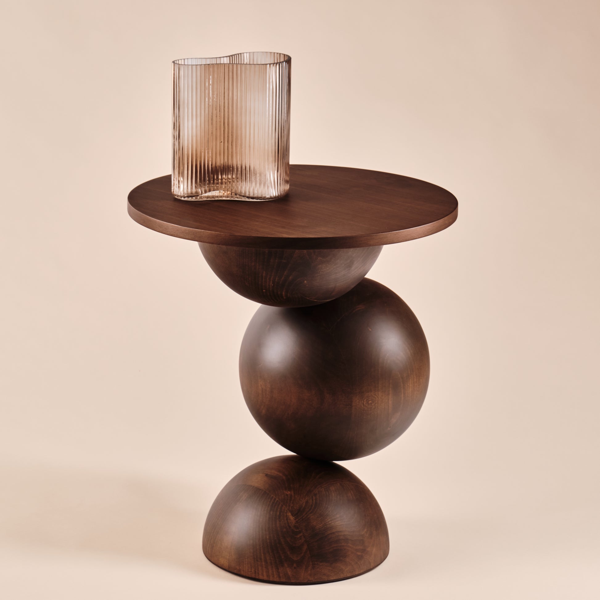 Beistelltisch Universe aus Holz mit runder Tischplatte und skulpturalem Design, dekoriert mit einer eleganten Glasvase in rauchiger Optik. Ein zeitloses Möbelstück, das Eleganz und Funktionalität in moderne Wohnräume bringt.