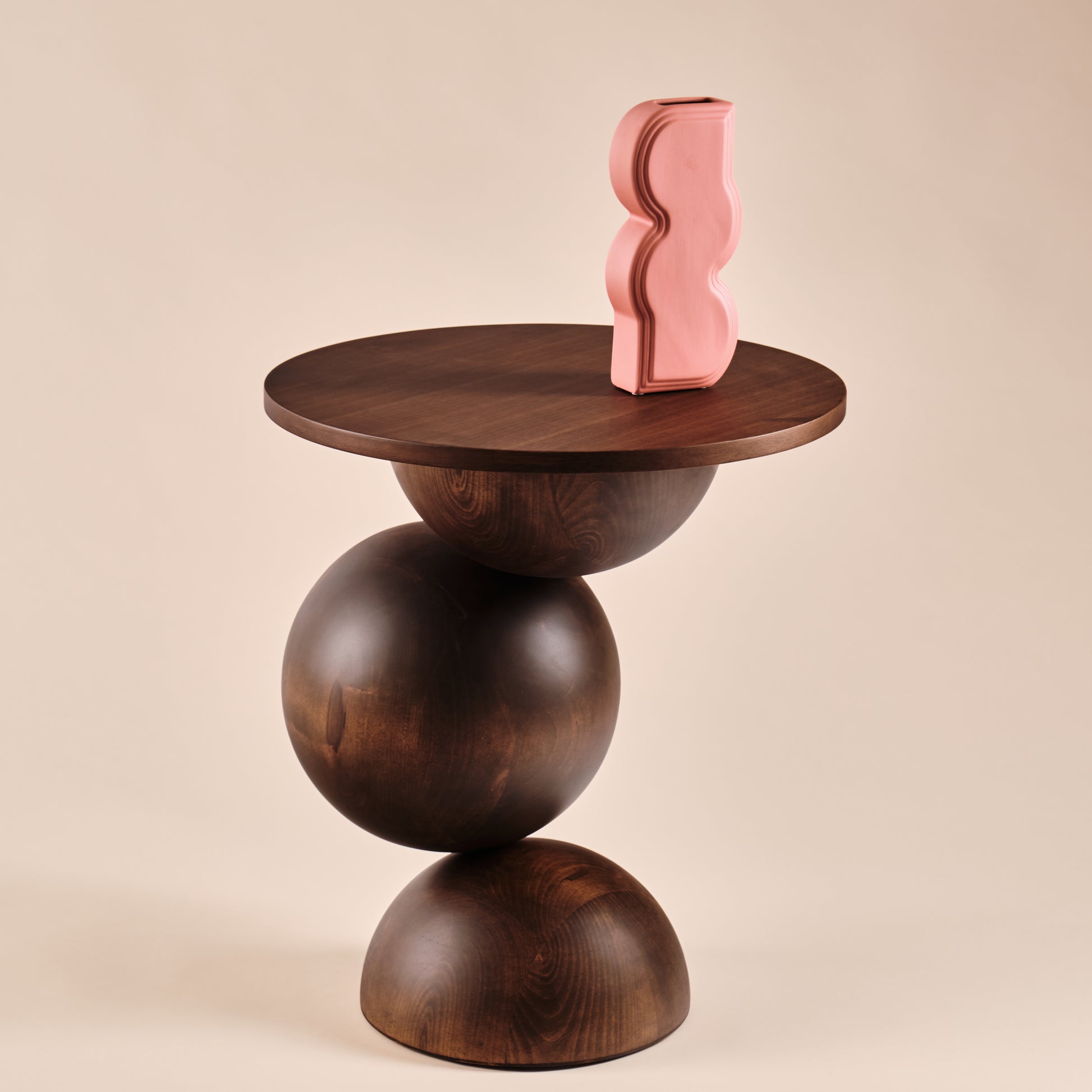 Beistelltisch Universe aus Holz mit runder Tischplatte und skulpturalem Design, dekoriert mit einer auffälligen pinken Vase in geschwungener Form. Ein elegantes Möbelstück, das Funktionalität und Ästhetik in zeitgenössische Wohnräume bringt.