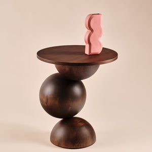 Beistelltisch Universe aus Holz mit runder Tischplatte und skulpturalem Design, dekoriert mit einer auffälligen pinken Vase in geschwungener Form. Ein elegantes Möbelstück, das Funktionalität und Ästhetik in zeitgenössische Wohnräume bringt.