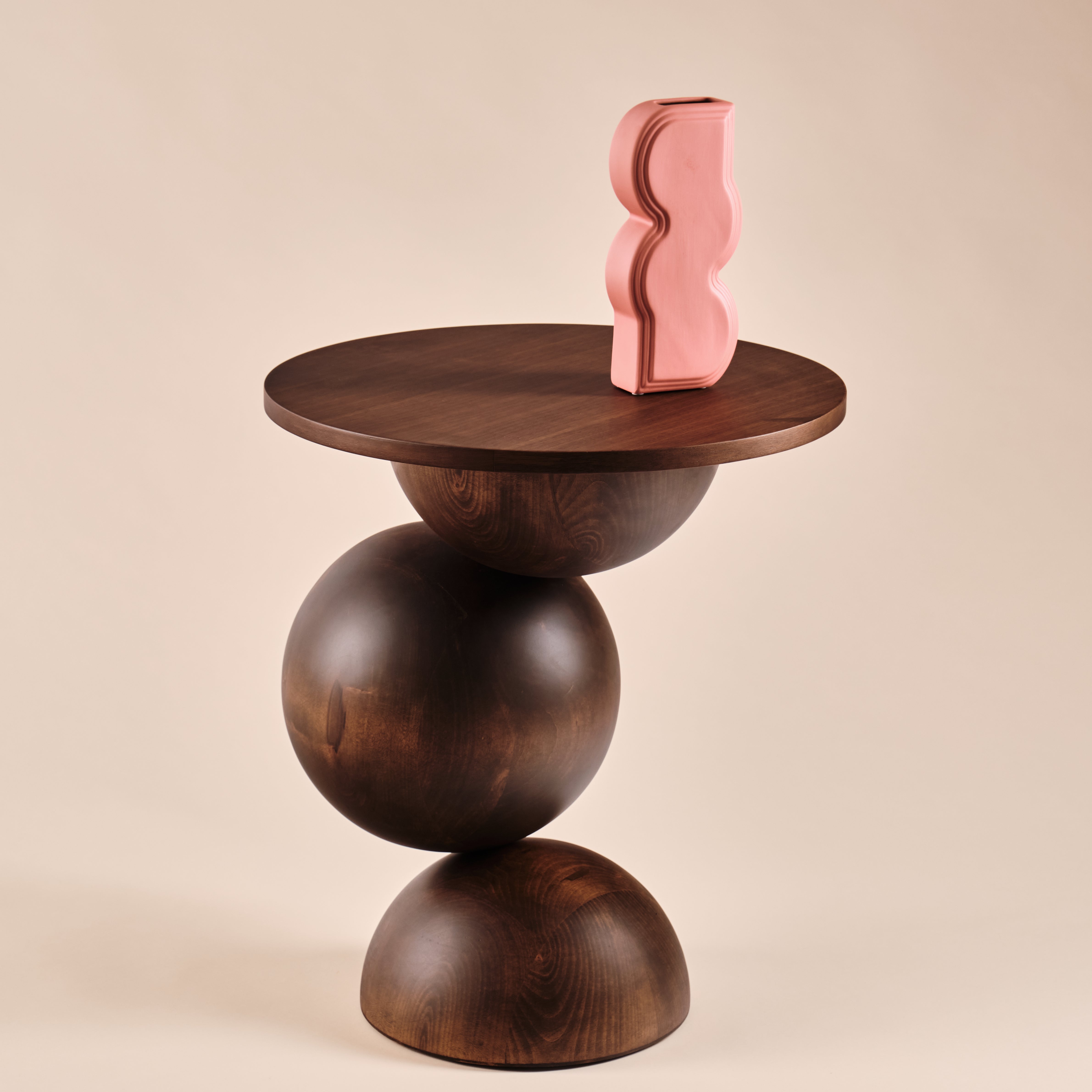 Beistelltisch Universe aus Holz mit runder Tischplatte und skulpturalem Design, dekoriert mit einer auffälligen pinken Vase in geschwungener Form. Ein elegantes Möbelstück, das Funktionalität und Ästhetik in zeitgenössische Wohnräume bringt.