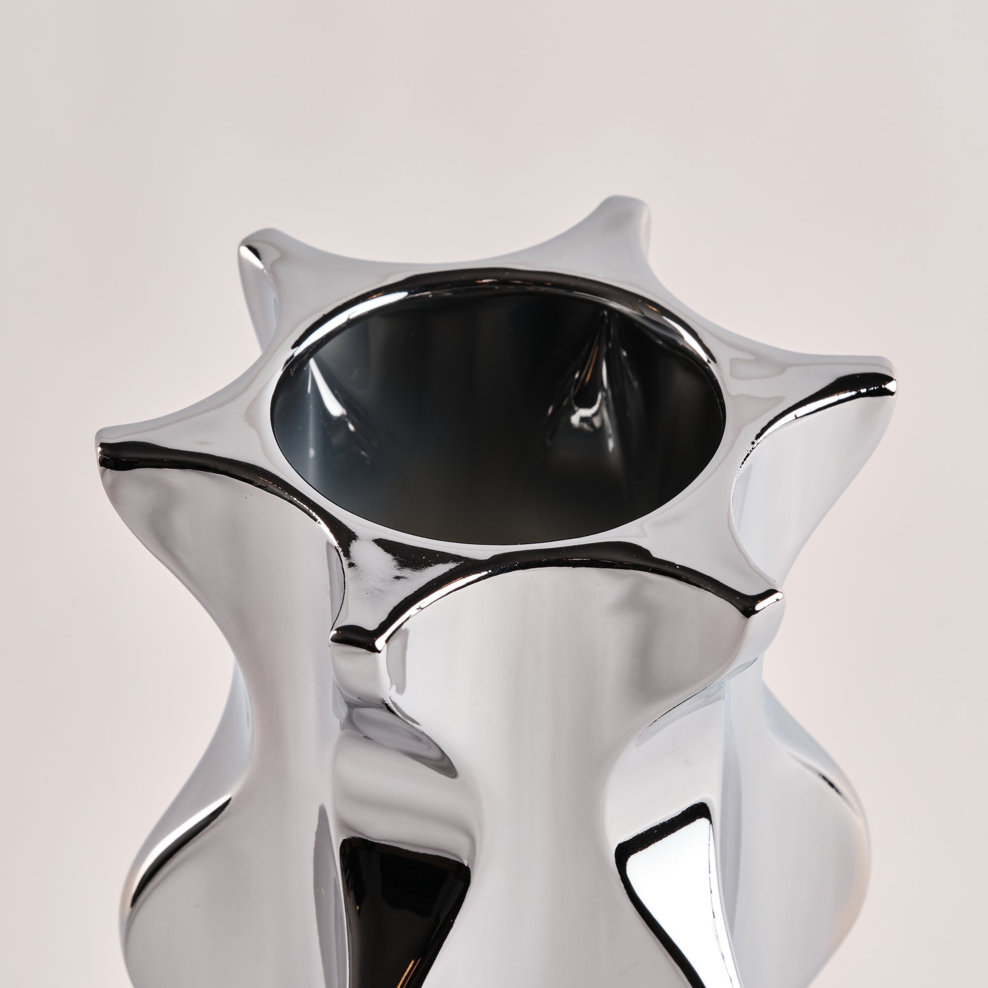 Nahaufnahme der Porzellanvase "Cactus" in glänzendem Chrom. Die auffällige, sternförmige Öffnung und die geschwungenen Kanten der Vase unterstreichen das elegante und moderne Design.