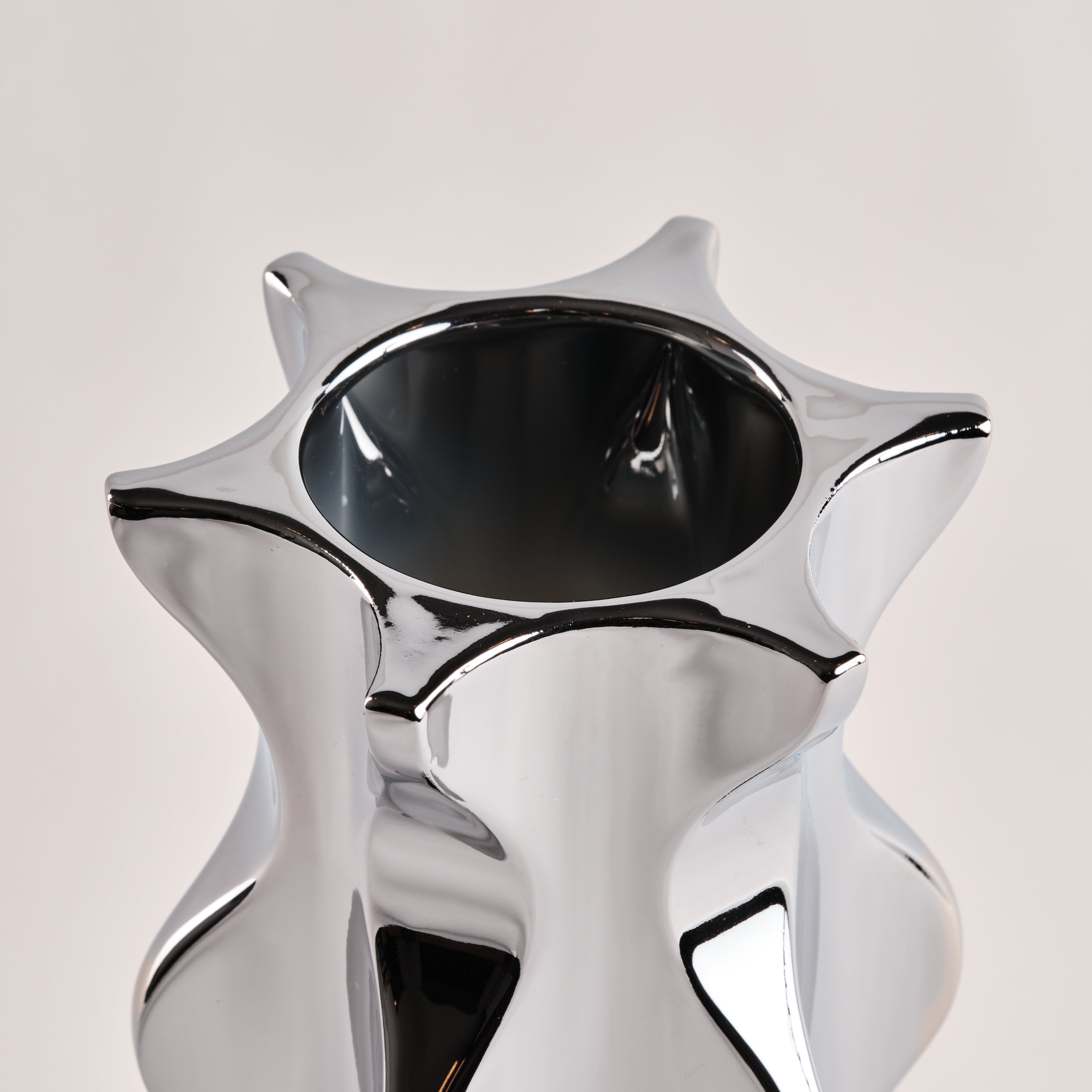 Nahaufnahme der Porzellanvase "Cactus" in glänzendem Chrom. Die auffällige, sternförmige Öffnung und die geschwungenen Kanten der Vase unterstreichen das elegante und moderne Design.