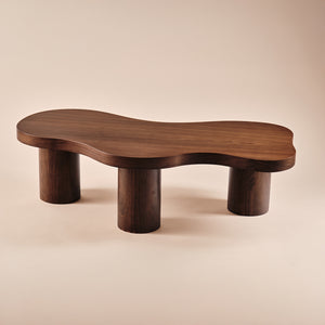 Couchtisch Sofie aus Holz mit organisch geformter Tischplatte und stabilen zylindrischen Beinen. Ein modernes und elegantes Möbelstück, das natürliche Ästhetik und Funktionalität in zeitgemäße Wohnzimmer bringt.