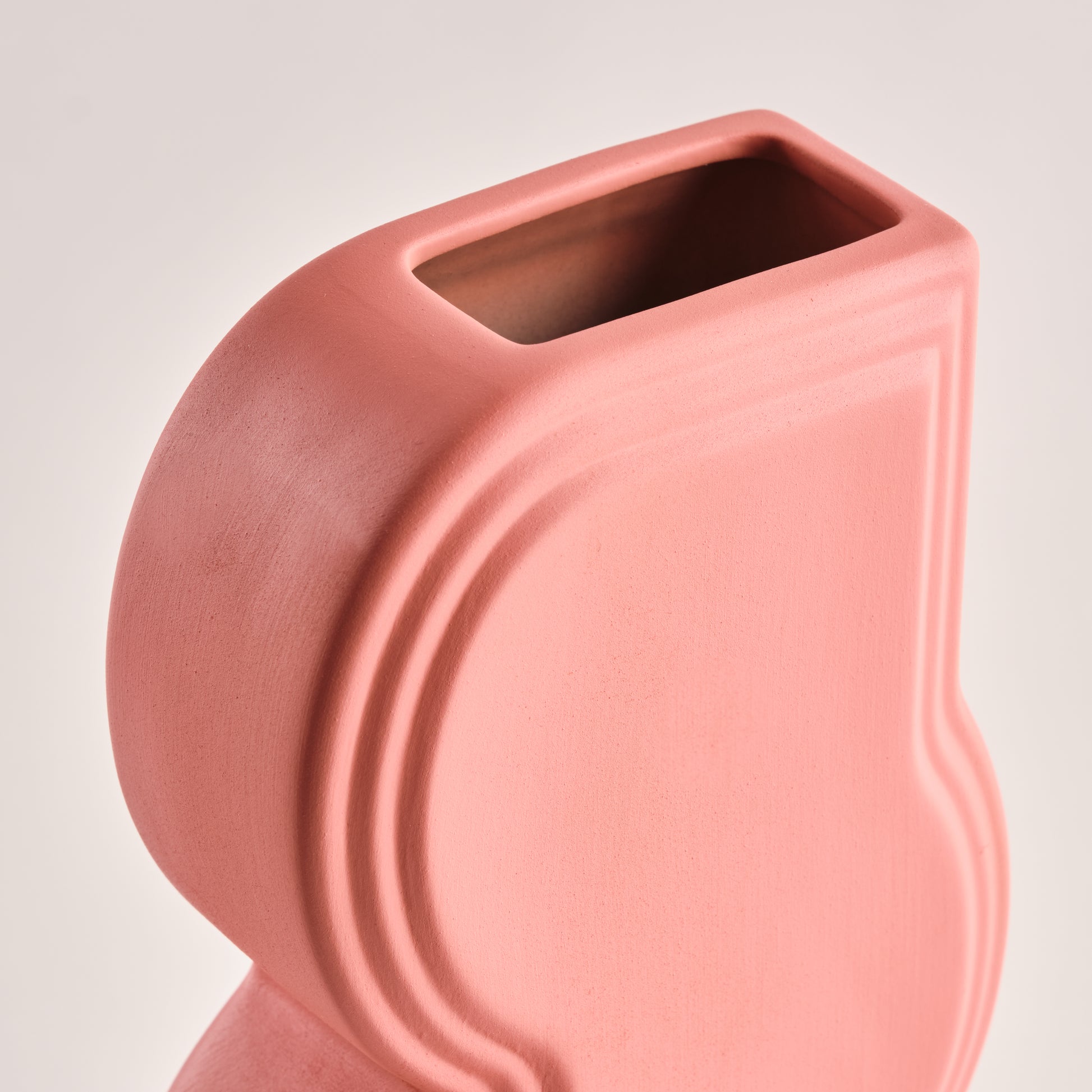 Nahaufnahme der modernen Porzellanvase "Whirl" in Korallrosa. Die geschwungenen Linien und das matte Finish betonen das raffinierte Design dieser einzigartigen Vase. Ideal als Deko-Highlight für zeitgenössische Wohnräume.