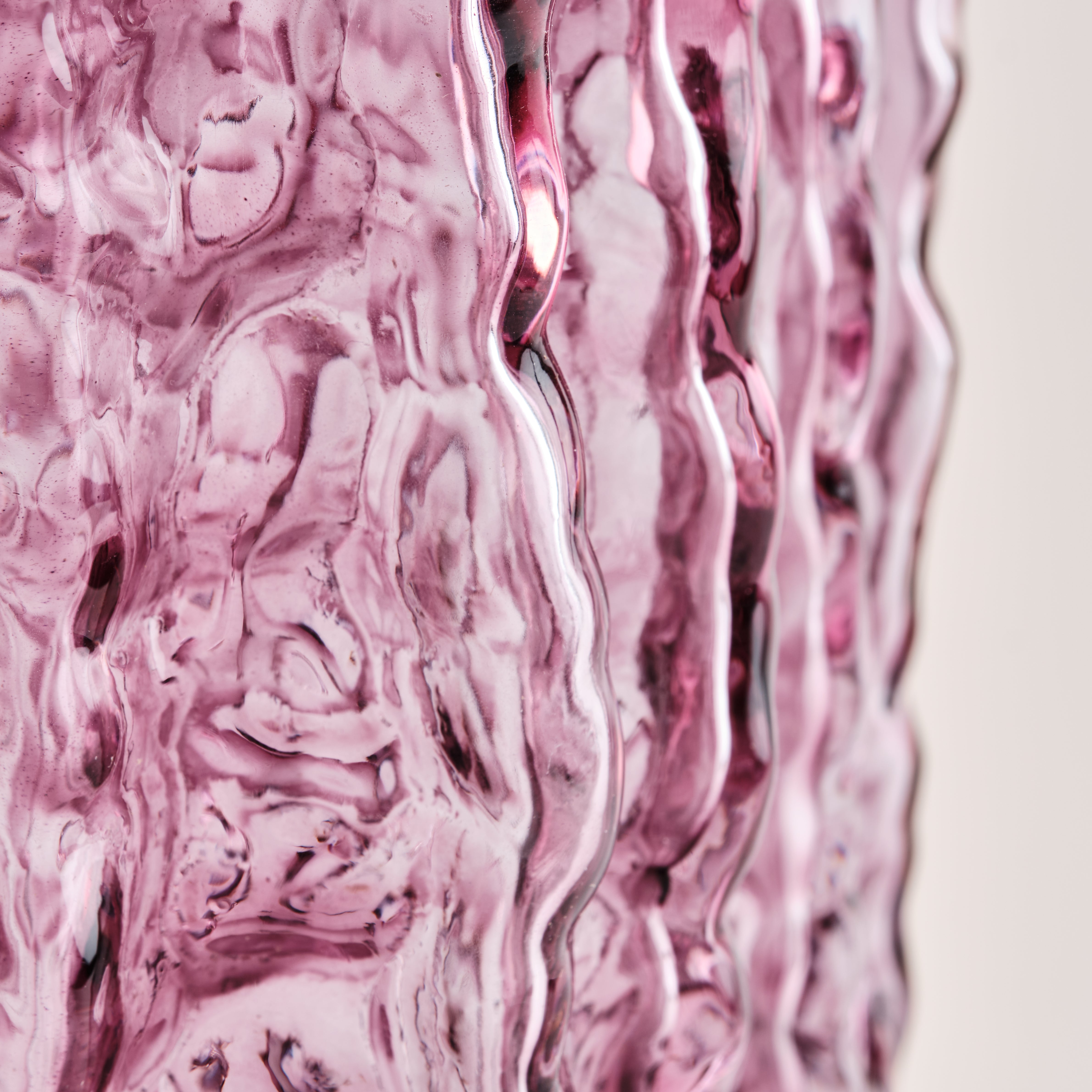 Nahaufnahme der Glasvase Raw in Rosa. Die wellenförmige, strukturierte Oberfläche reflektiert das Licht und betont das kunstvolle, handgefertigte Design der Vase.